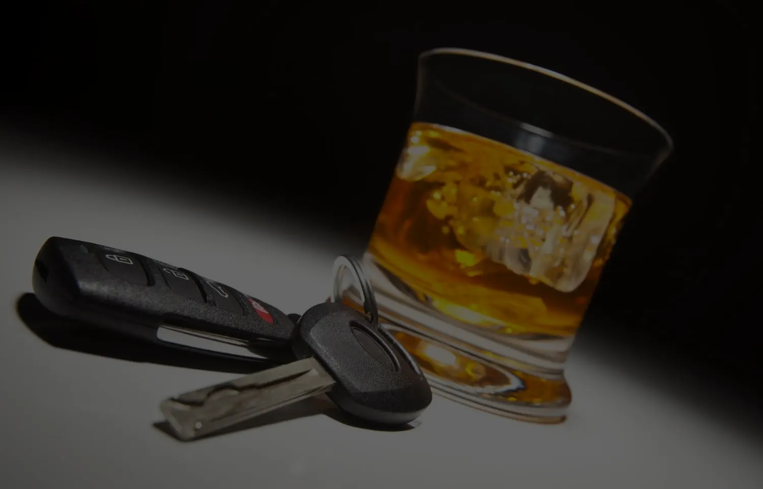 Car keys on a table next to a glass of whisky, representing the road back to a licence after a DUI